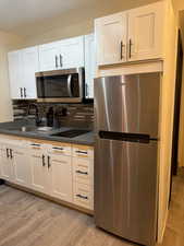 Kitchen with white cabinets, light hardwood / wood-style floors, stainless steel appliances, and sink