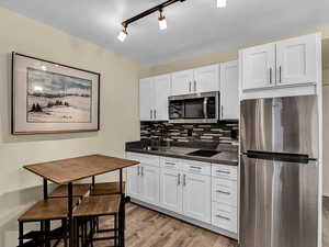 Kitchen featuring stainless steel appliances, decorative backsplash, light hardwood / wood-style floors, sink, and white cabinetry