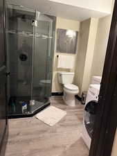 Bathroom featuring hardwood / wood-style flooring, a shower with door, toilet, and washer / dryer