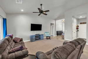 Living room with ceiling fan with notable chandelier, vaulted ceiling, and light colored carpet