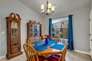 Dining area with lofted ceiling, light tile patterned floors, and a notable chandelier