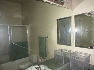 Bathroom with bath / shower combo with glass door and toilet