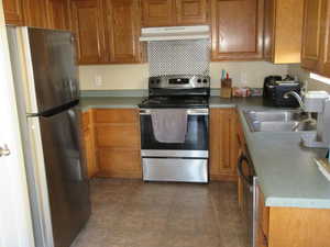 Kitchen with sink, dark tile patterned flooring, stainless steel appliances, and range hood