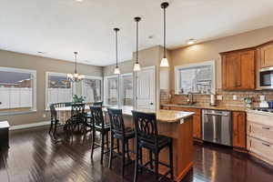 Kitchen featuring stainless steel appliances, light stone counters, decorative light fixtures, a center island, and sink