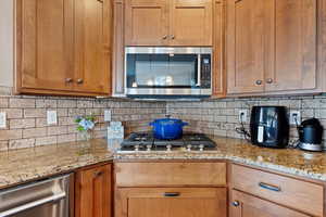 Kitchen featuring appliances with stainless steel finishes, light stone countertops, and decorative backsplash