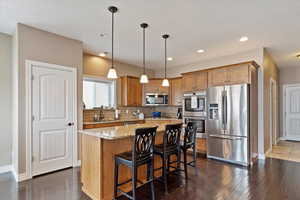 Kitchen featuring hanging light fixtures, a center island, light stone countertops, tasteful backsplash, and appliances with stainless steel finishes