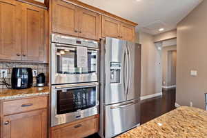 Kitchen featuring tasteful backsplash, stainless steel appliances, light stone countertops, and dark wood-type flooring