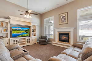 Carpeted living room with ceiling fan, vaulted ceiling, and a high end fireplace