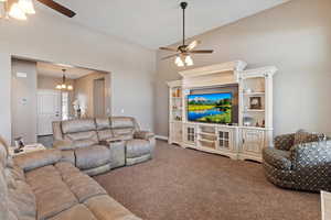 Living room featuring ceiling fan with notable chandelier, carpet, and high vaulted ceiling