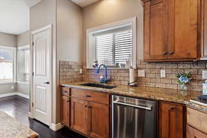 Kitchen with stainless steel dishwasher, sink, light stone counters, and backsplash