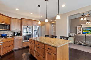 Kitchen with stainless steel appliances, decorative light fixtures, a kitchen island, light stone counters, and decorative backsplash