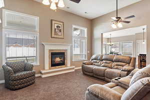 Carpeted living room featuring ceiling fan with notable chandelier, plenty of natural light, and a tile fireplace