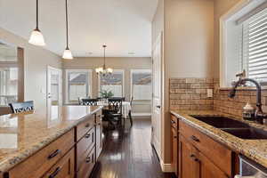 Kitchen with sink, light stone counters, decorative light fixtures, dark hardwood / wood-style flooring, and decorative backsplash