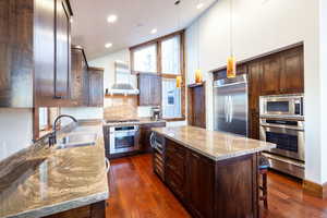 Kitchen featuring a center island, built in appliances, light stone countertops, sink, and wall chimney range hood