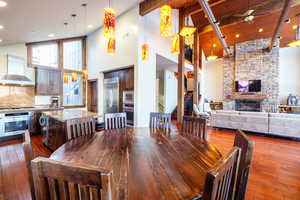 Dining space featuring a stone fireplace, ceiling fan, high vaulted ceiling, hardwood / wood-style floors, and beamed ceiling