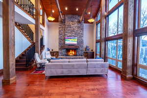 Living room with beam ceiling, wood-type flooring, a stone fireplace, and a towering ceiling