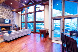 Living room featuring beam ceiling, wood-type flooring, a stone fireplace, high vaulted ceiling, and wooden ceiling