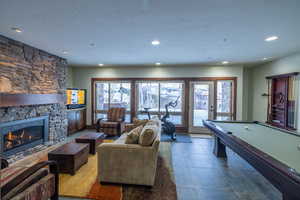 Rec room featuring a textured ceiling, billiards, a stone fireplace, and tile patterned floors