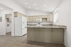 Kitchen featuring white appliances, a peninsula, light stone counters, baseboards, and lofted ceiling