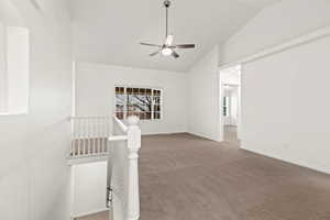 Carpeted empty room with vaulted ceiling, a ceiling fan, and baseboards