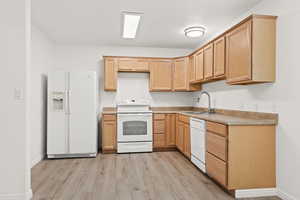 Kitchen with white appliances, a sink, light wood-style flooring, light brown cabinetry, and light countertops