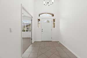Entrance foyer with a chandelier, baseboards, light tile patterned floors, and light colored carpet