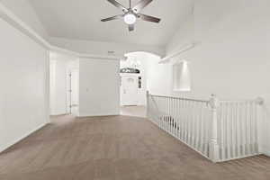 Unfurnished room featuring carpet floors, a ceiling fan, arched walkways, baseboards, and vaulted ceiling