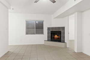 Unfurnished living room featuring ceiling fan, a tile fireplace, light tile patterned floors, and baseboards