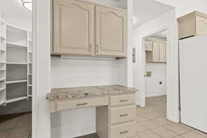 Kitchen featuring freestanding refrigerator, cream cabinetry, light tile patterned floors, and light stone countertops