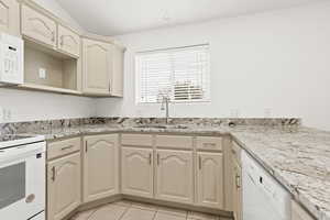 Kitchen with white appliances, a sink, cream cabinets, light tile patterned floors, and light stone countertops