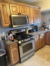 Kitchen with dark stone counters, appliances with stainless steel finishes, and light tile patterned flooring