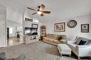 Carpeted living room with ceiling fan and lofted ceiling