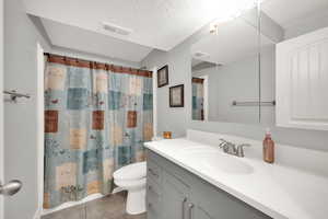 Bathroom featuring tile patterned flooring, toilet, a shower with curtain, a textured ceiling, and vanity