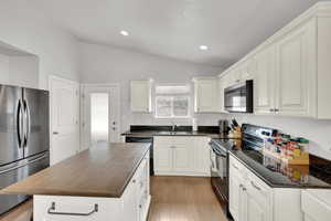 Kitchen with white cabinets, vaulted ceiling, black appliances, and a kitchen island