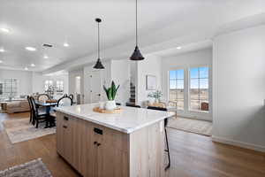 Kitchen featuring hanging light fixtures, wood-type flooring, light stone counters, a breakfast bar, and a kitchen island