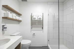 Bathroom with hardwood / wood-style floors, radiator heating unit, vanity, tiled shower, and toilet