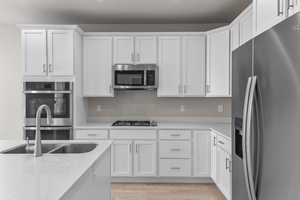Kitchen featuring white cabinetry, stainless steel appliances, light stone countertops, light hardwood / wood-style floors, and sink