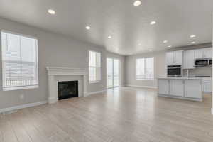 Unfurnished living room featuring light hardwood / wood-style flooring, a textured ceiling, and a healthy amount of sunlight