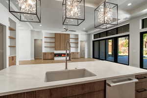 Kitchen featuring built in shelves, dishwasher, a large fireplace, pendant lighting, and sink