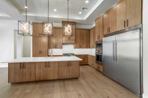 Kitchen with a raised ceiling, built in appliances, sink, and a large island with sink