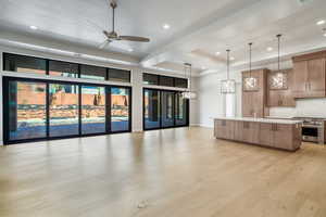 Kitchen with light wood-type flooring, ceiling fan, a spacious island, hanging light fixtures, and stainless steel stove