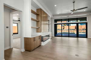 Interior space with a large fireplace, built in shelves, ceiling fan, and light hardwood / wood-style flooring