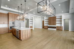 Kitchen featuring pendant lighting, light hardwood / wood-style floors, a spacious island, and a raised ceiling