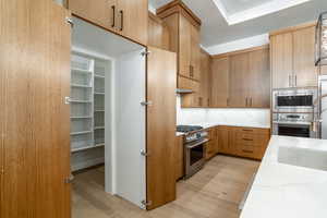 Kitchen with light hardwood / wood-style flooring, stainless steel appliances, light stone countertops, and sink