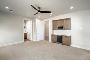 Interior space with light carpet, ceiling fan, beverage cooler, and stainless steel microwave