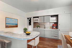 Kitchen featuring dark wood-style floors, backsplash, a breakfast bar area, and gray cabinets