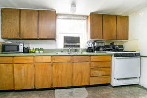 Kitchen featuring white gas range oven, stainless steel microwave, tile patterned floors, light countertops, and brown cabinets