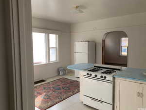 Kitchen with white appliances, arched walkways, white cabinets, light tile patterned flooring, and light countertops