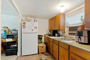 Kitchen with light tile patterned floors, sink, white fridge, and a textured ceiling