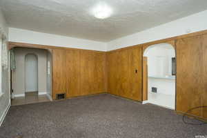 Unfurnished room with arched walkways, carpet flooring, a textured ceiling, and a smoke detector